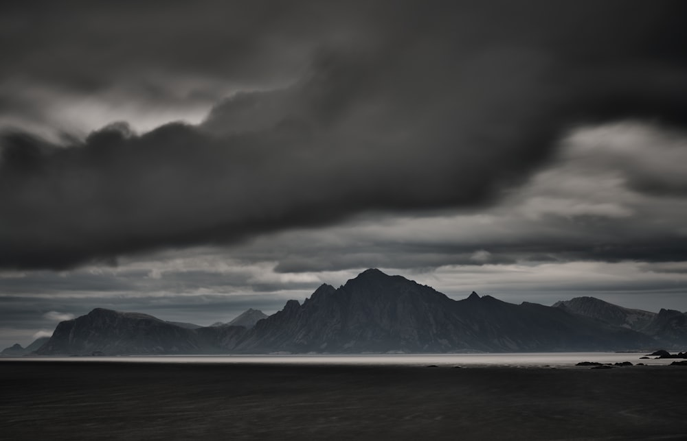 body of water near mountain under cloudy sky during daytime