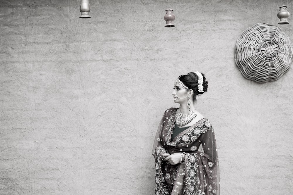 mulher em sari vermelho e marrom de pé ao lado da parede branca