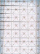 A symmetrical pattern with ornate, geometric designs featuring intricately detailed floral motifs spread across a grid-like layout. The motifs are enclosed within individual squares, with each square bordered by thin lines. The overall pattern has a classic and decorative aesthetic, reminiscent of an architectural ceiling or tiled surface.