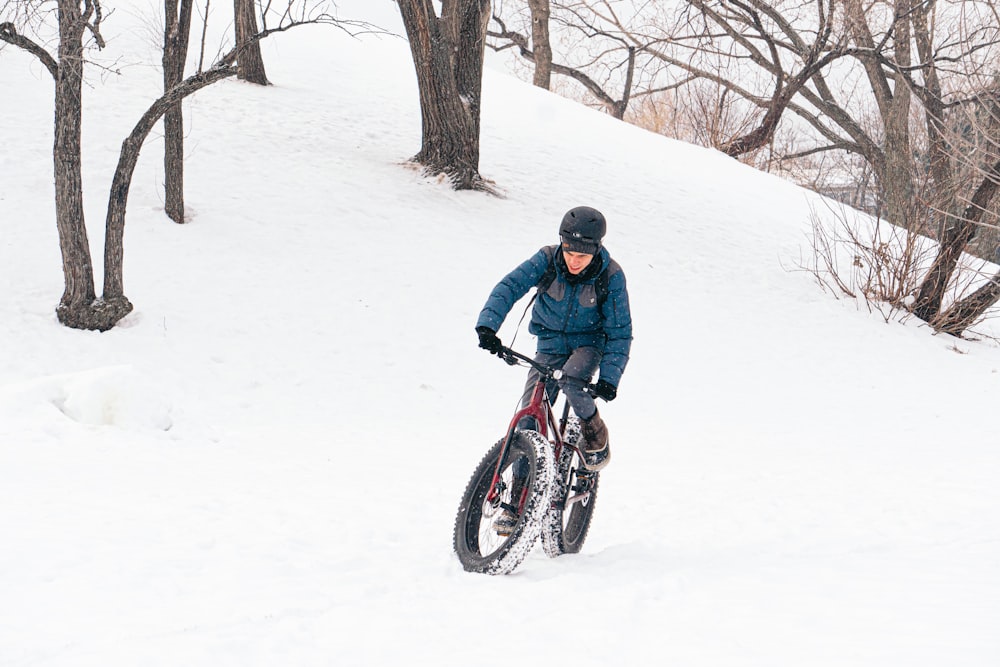man in black jacket riding on black and red bicycle on snow covered ground during daytime