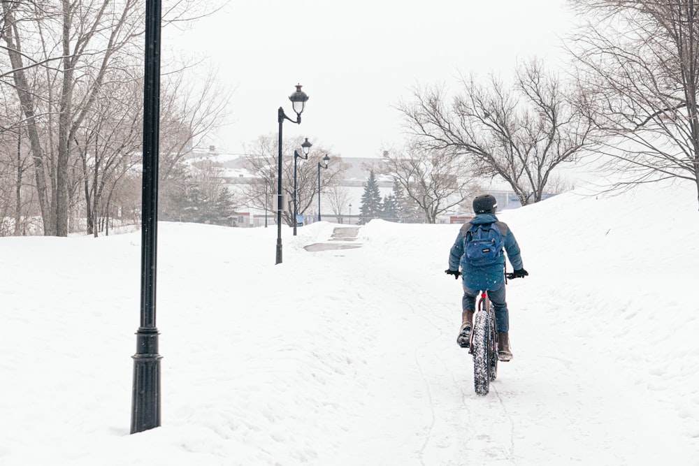 Hombre en chaqueta azul montando en bicicleta en terreno cubierto de nieve durante el día