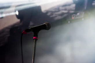 A close-up of a microphone with a softly lit stage background, ready for poets.