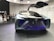 A futuristic concept car with a sleek design and gullwing doors open, showcasing advanced technology and stylish aesthetics. A group of people are observing and taking pictures, indicating a public exhibition or auto show setting.