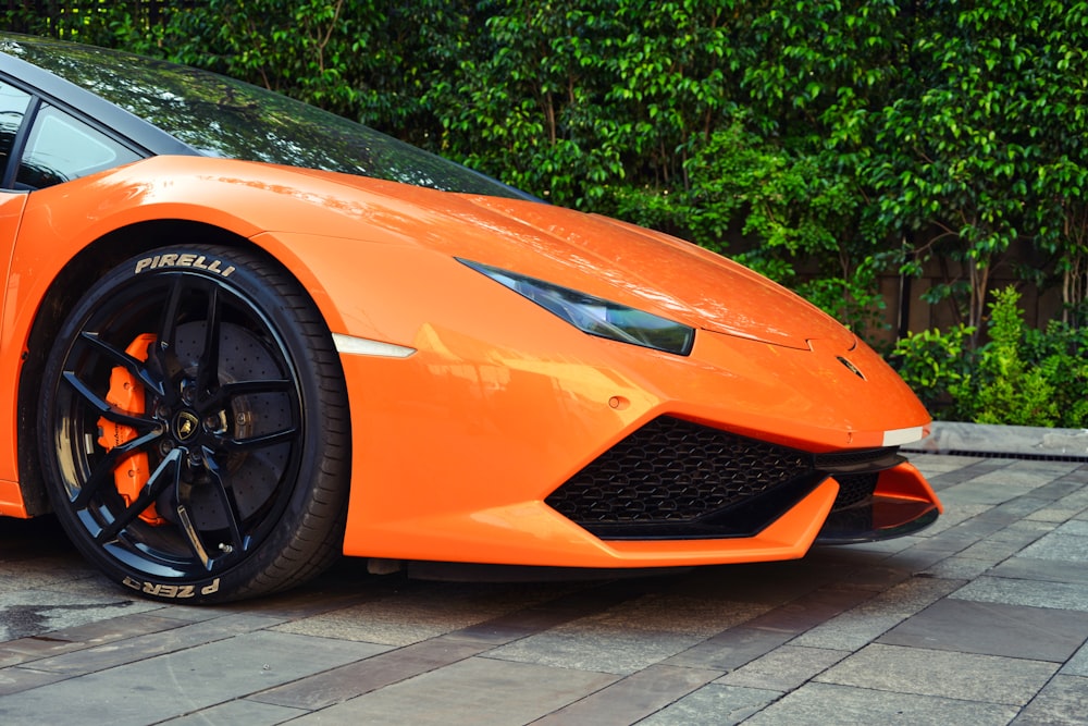 Coche Ferrari naranja aparcado cerca de plantas de hojas verdes durante el día