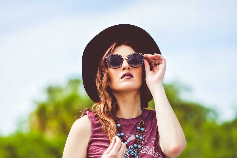 girl in purple and white floral tank top wearing black sun hat and black sunglasses