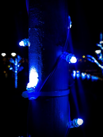A series of vibrant blue LED lights are wrapped around a vertical pole, casting a strong glow in the dark surroundings. Additional lights can be seen in the background, creating a festive atmosphere.
