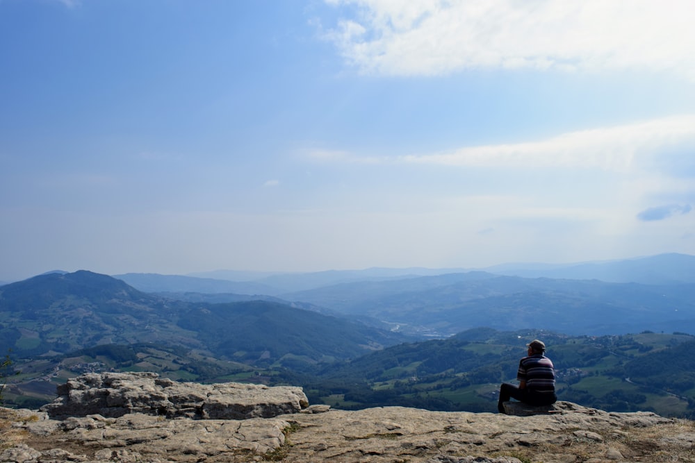 person sitting on rock formation looking at mountains during daytime