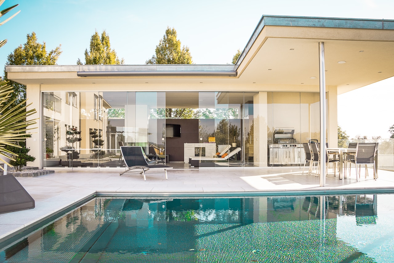 Luxury villa terrace featuring Grade-A teak outdoor dining furniture, powder-coated aluminium lounge seating with Sunbrella solution-dyed acrylic cushions in warm sand tones, and architectural landscape lighting — creating seamless material continuity between indoor and outdoor living spaces