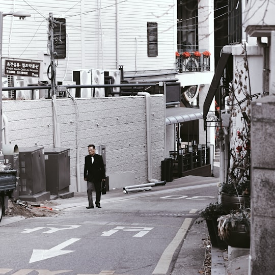 man in black jacket walking on sidewalk during daytime in Myeongdong-gil South Korea