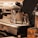 A shiny metal espresso machine with two small stainless steel milk pitchers placed on the drip tray, surrounded by dials and levers. The machine has a polished chrome surface with black handles and knobs, reflecting a warm light.
