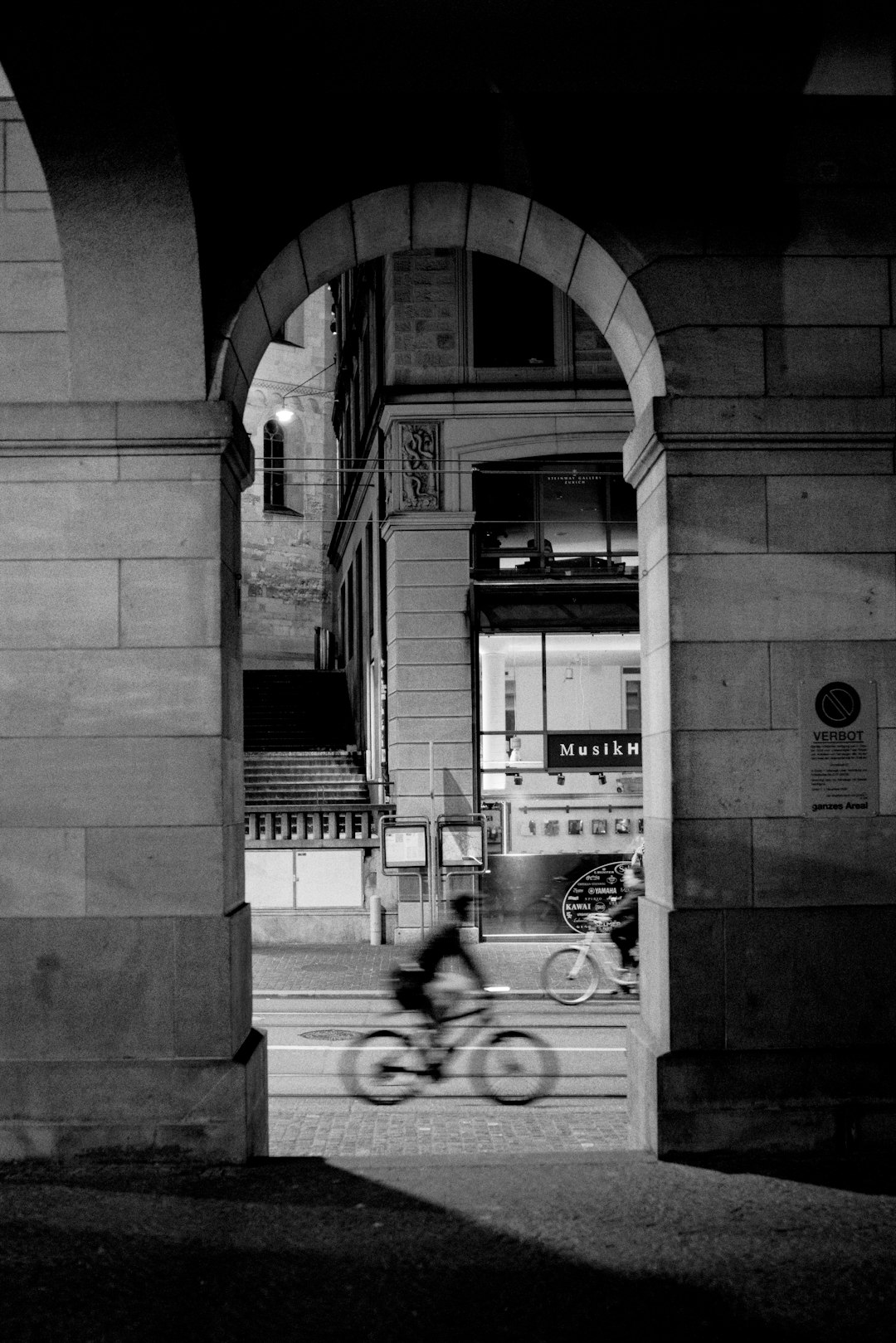 grayscale photo of man riding bicycle near building