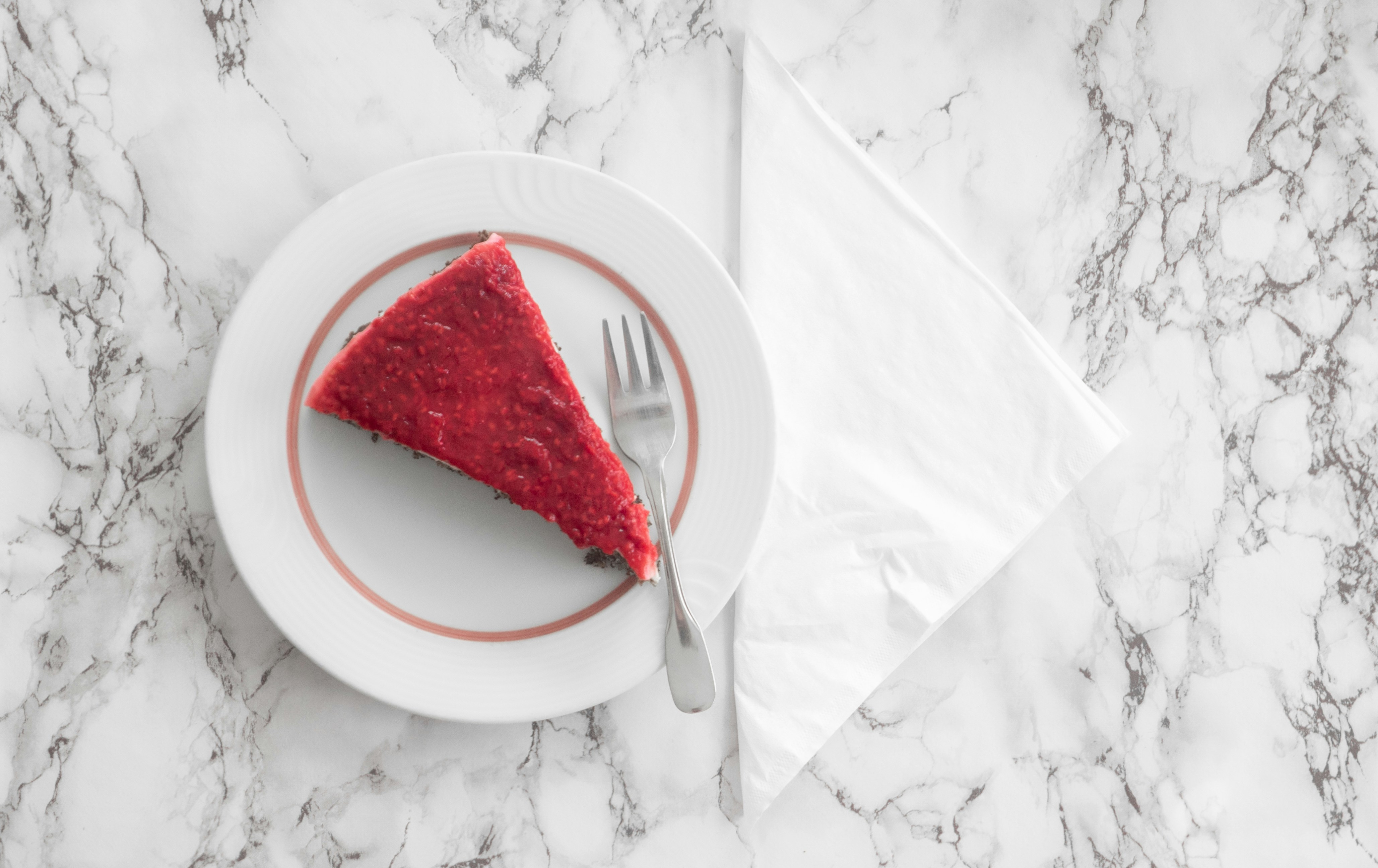 Irisan kue red velvet, warna merah cerah, pencahayaan bakery terang, permukaan putih bersih