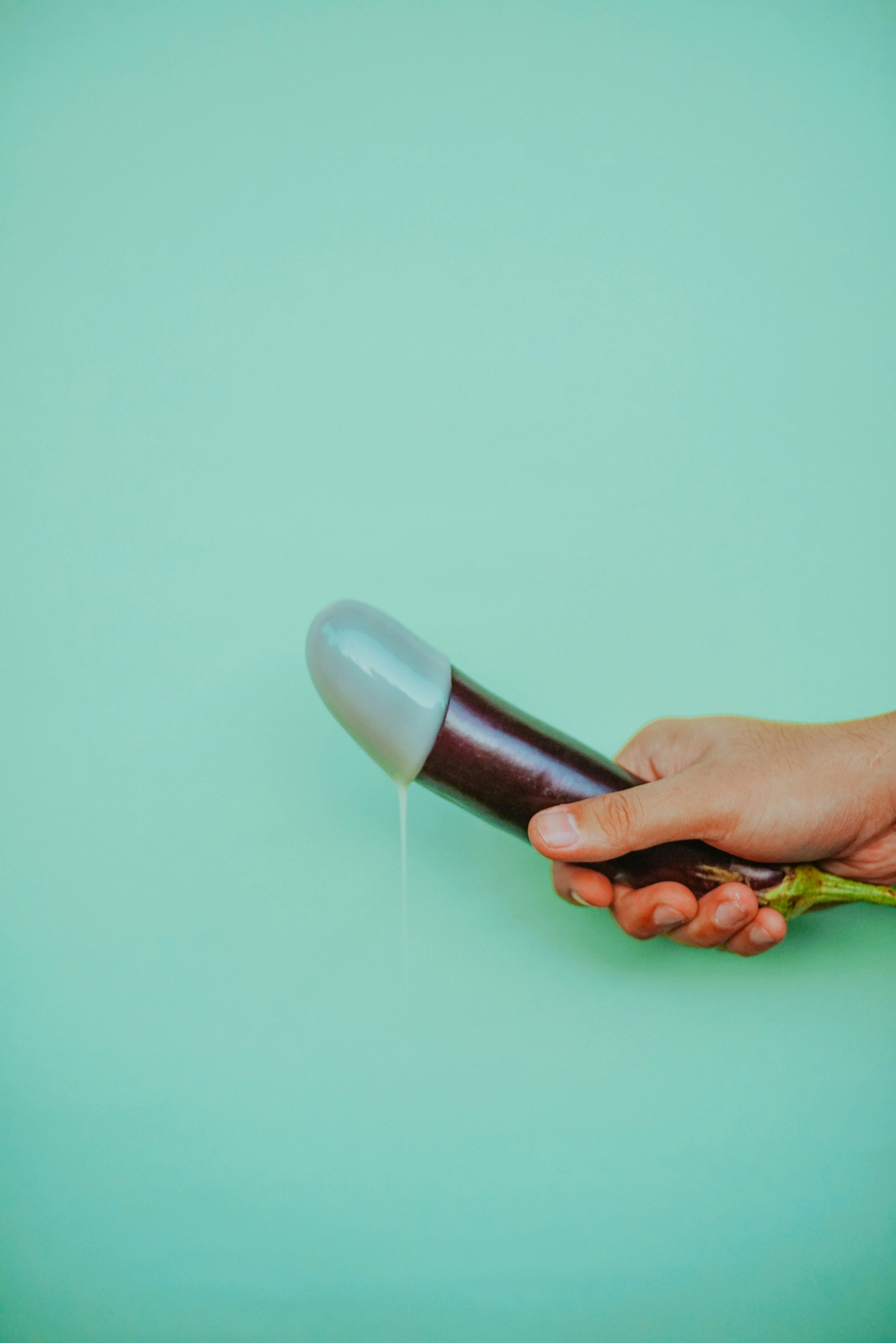 A hand holding an eggplant with a milky substance at the tip of the eggplant.