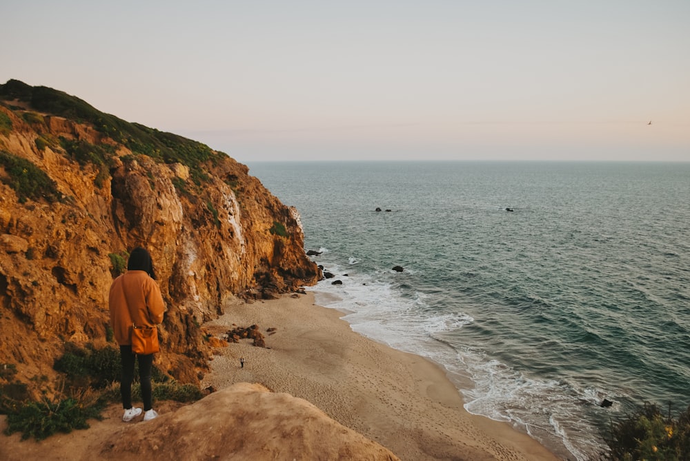 2 person standing on brown rock formation near body of water during daytime