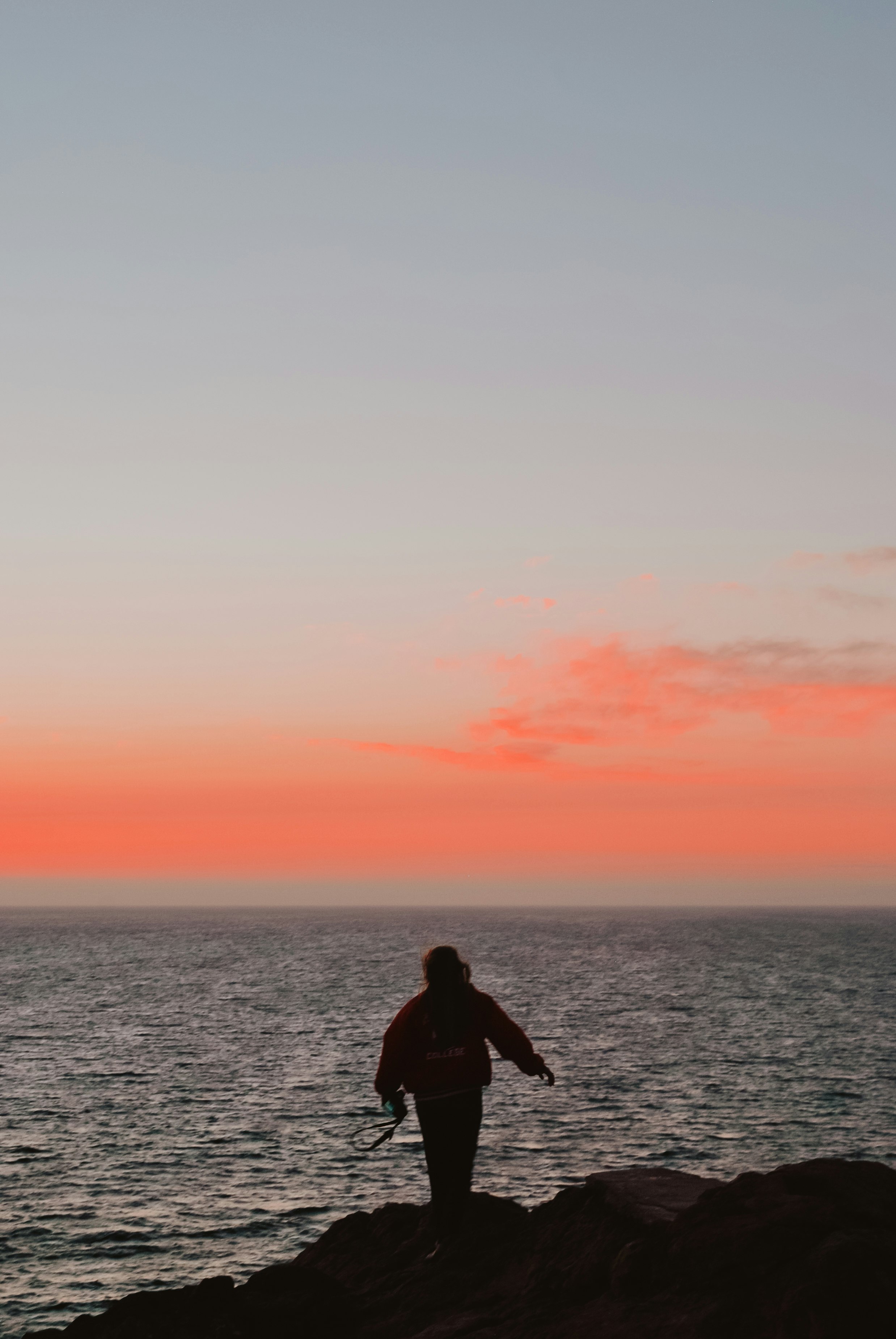 man in black jacket standing on the sea during sunset