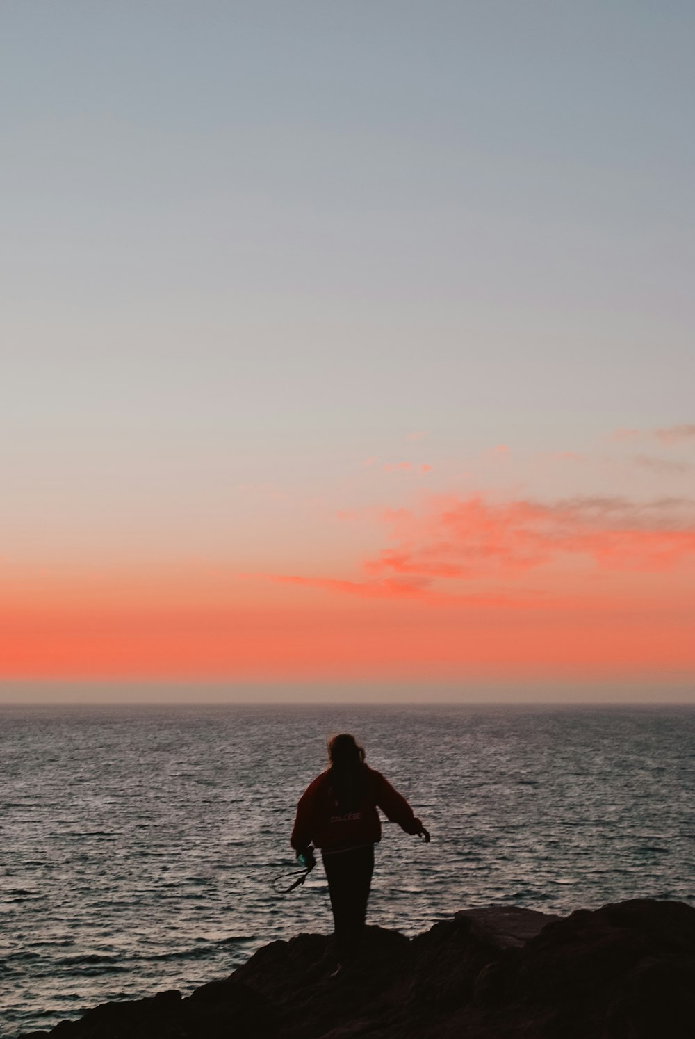 man in black jacket standing on the sea during sunset