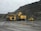 Heavy mining machinery is situated in a rocky terrain with piles of earth and rock in the background. There are three large vehicles, including a dump truck, a large excavator, and another piece of mining equipment.