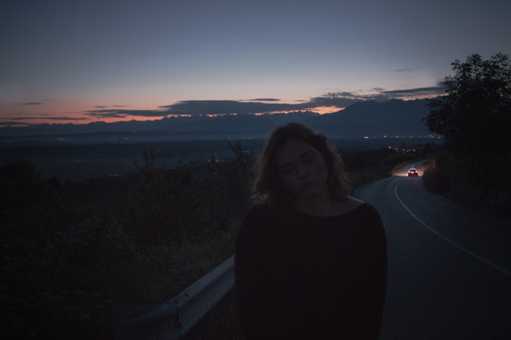Frau im schwarzen Rollkragenpullover steht bei Sonnenuntergang auf dem Gipfel des Berges