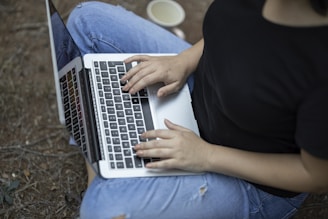 person in black shirt and blue denim jeans using macbook air