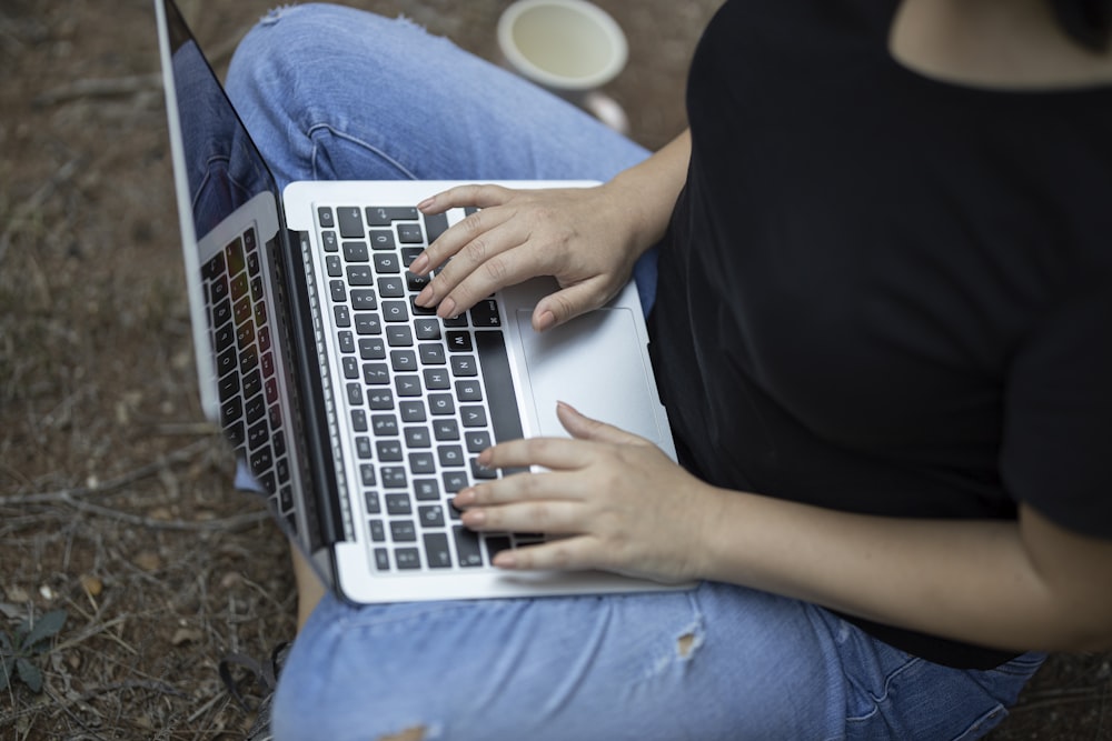 person in black shirt and blue denim jeans using macbook air