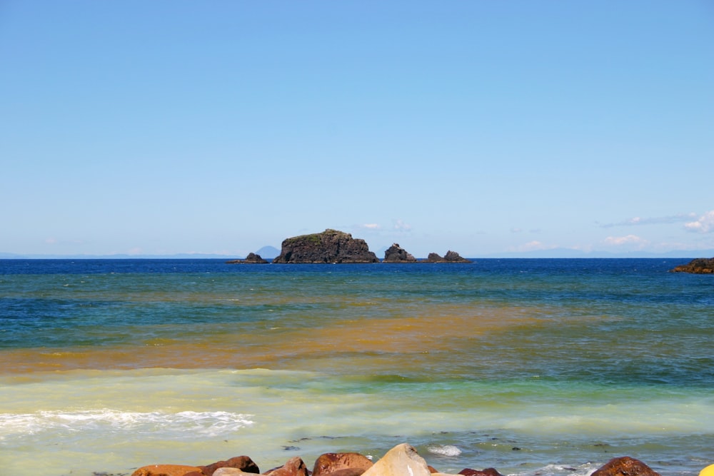 brown rock formation on sea under blue sky during daytime