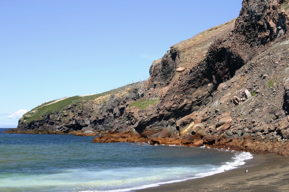 Formation rocheuse brune et verte au bord de la mer bleue sous le ciel bleu pendant la journée