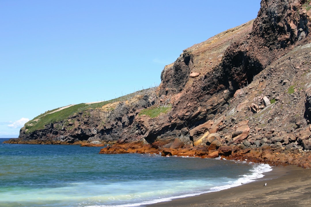 brown and green rock formation beside blue sea under blue sky during daytime