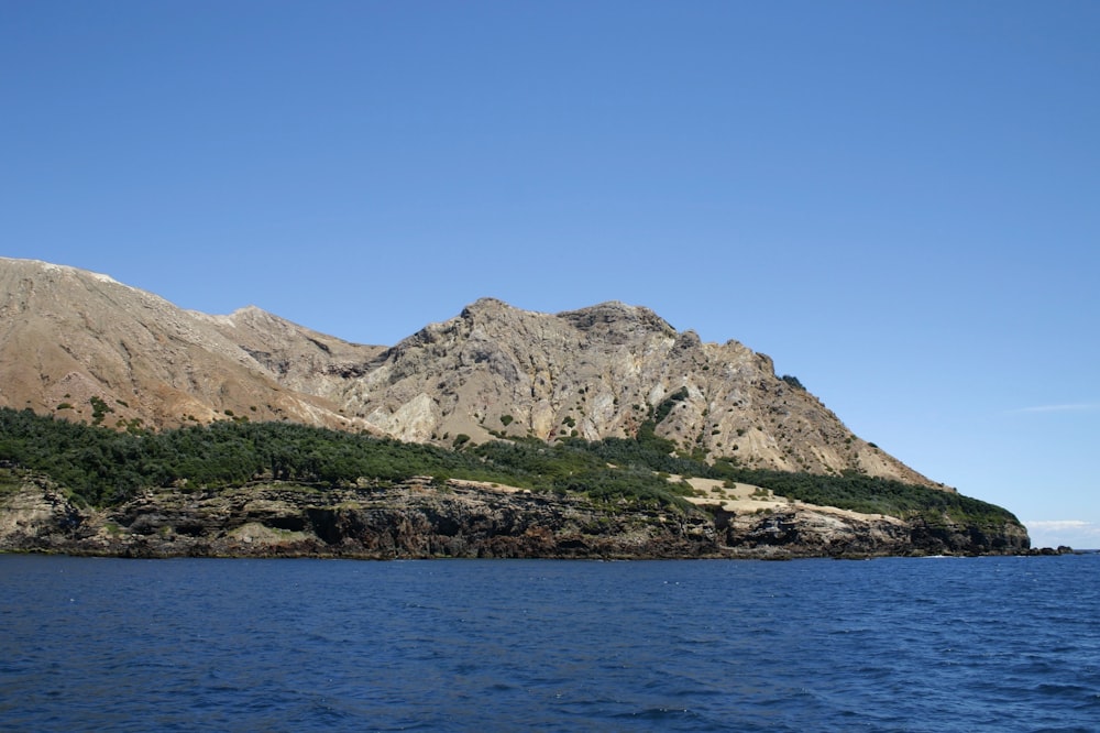 brown and green mountain beside body of water during daytime