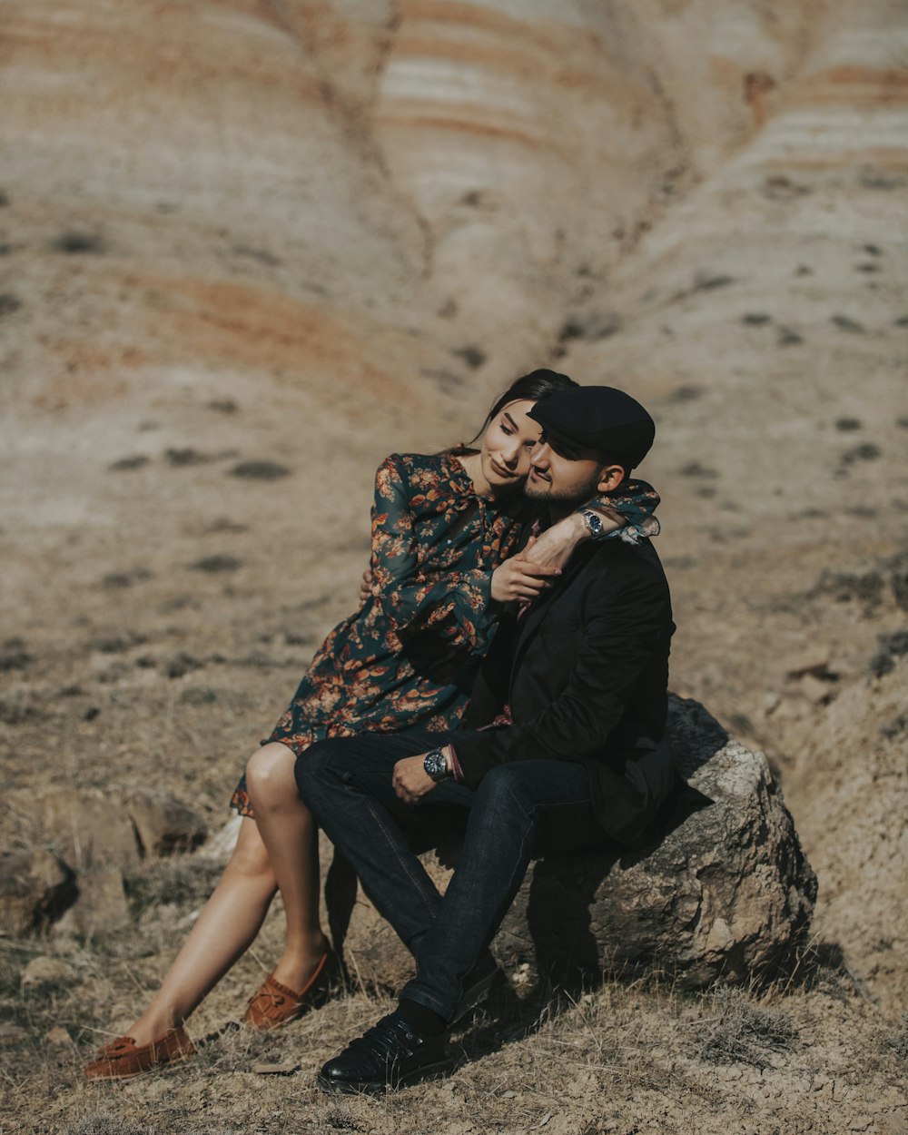 man in black and brown floral shirt and black pants sitting on rock during daytime