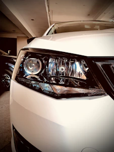 A close-up of a car's headlight being carefully restored to a crystal-clear finish under bright workshop lights.