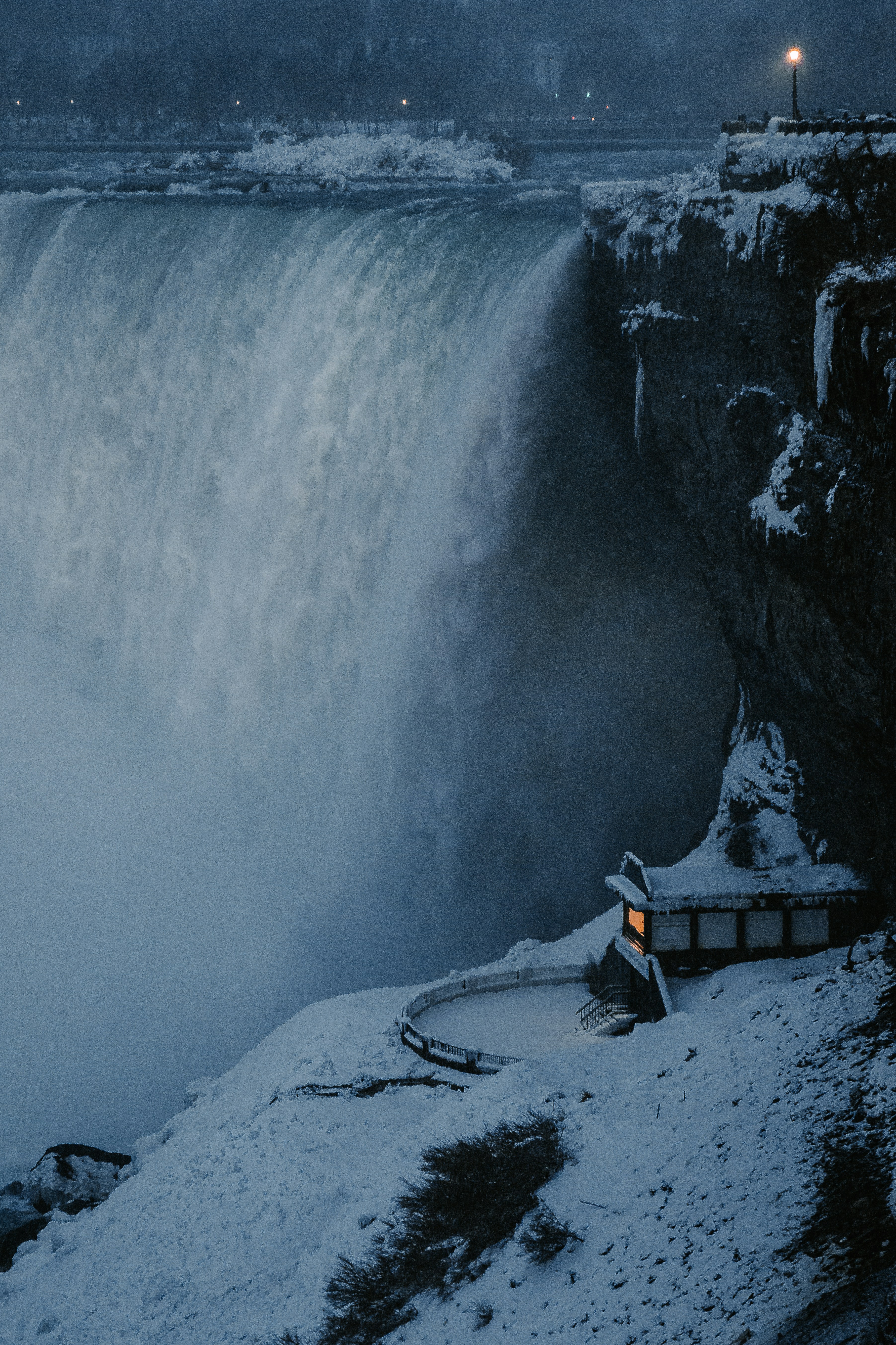 Person sitzt tagsüber auf einer braunen Holzbank vor Wasserfällen