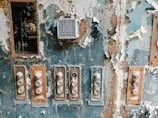 A weathered and rusty control panel with peeling paint and multiple buttons that appear worn. The buttons are arranged in a vertical fashion with labels like 'START'. A small vent or speaker is visible above the buttons. The surrounding paint is flaking off, revealing rust underneath.