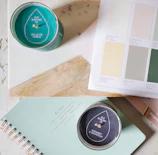 A serene flat lay of a cream journal, gold pen, and a softly glowing candle on a white surface.