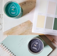 A minimalist flat lay of a warm taupe linen journal, a smooth stone gray candle, and a muted sage ceramic cup.