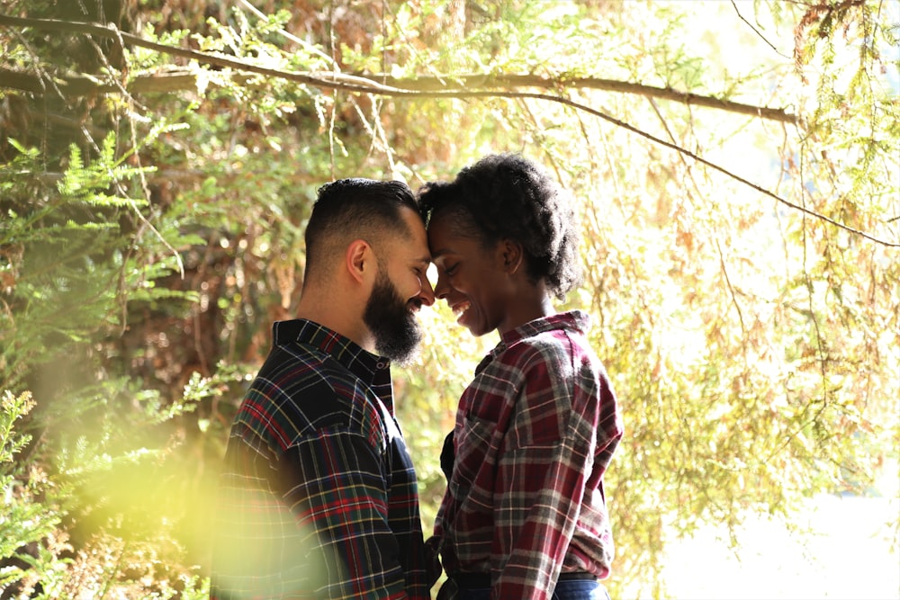 man and woman kissing near green trees during daytime