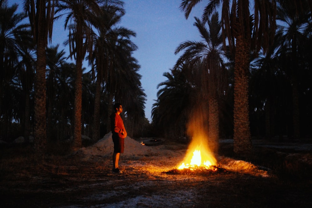 man in red jacket standing near bonfire during night time