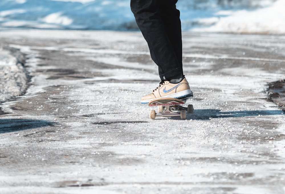 person in black pants and brown and white nike sneakers standing on gray sand during daytime