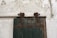 A rustic wooden door with a faded green color and metal hinges is mounted on a textured, peeling white wall. The door has a set of industrial-looking metal fixtures that suggest it slides to open. Above the door, there is a set of numbers painted directly on the wall.