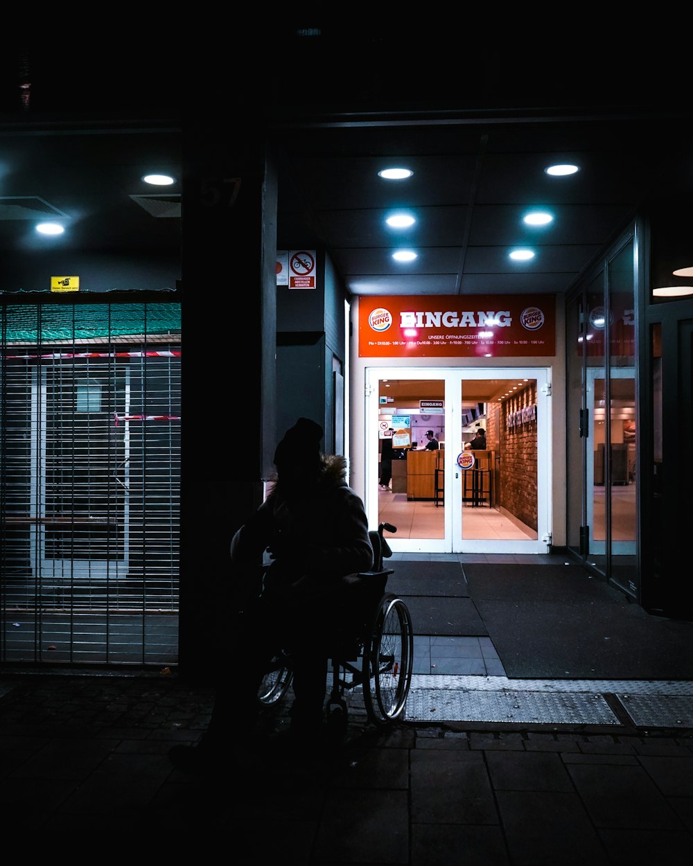 femme en manteau noir debout près du magasin rouge et blanc pendant la nuit