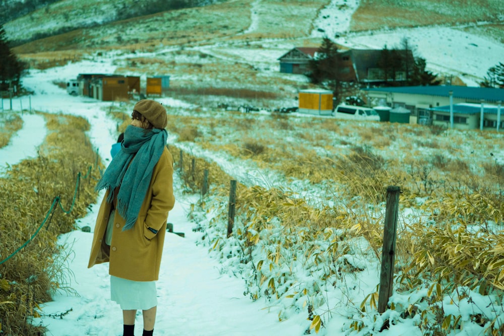 woman in brown coat standing on snow covered field during daytime