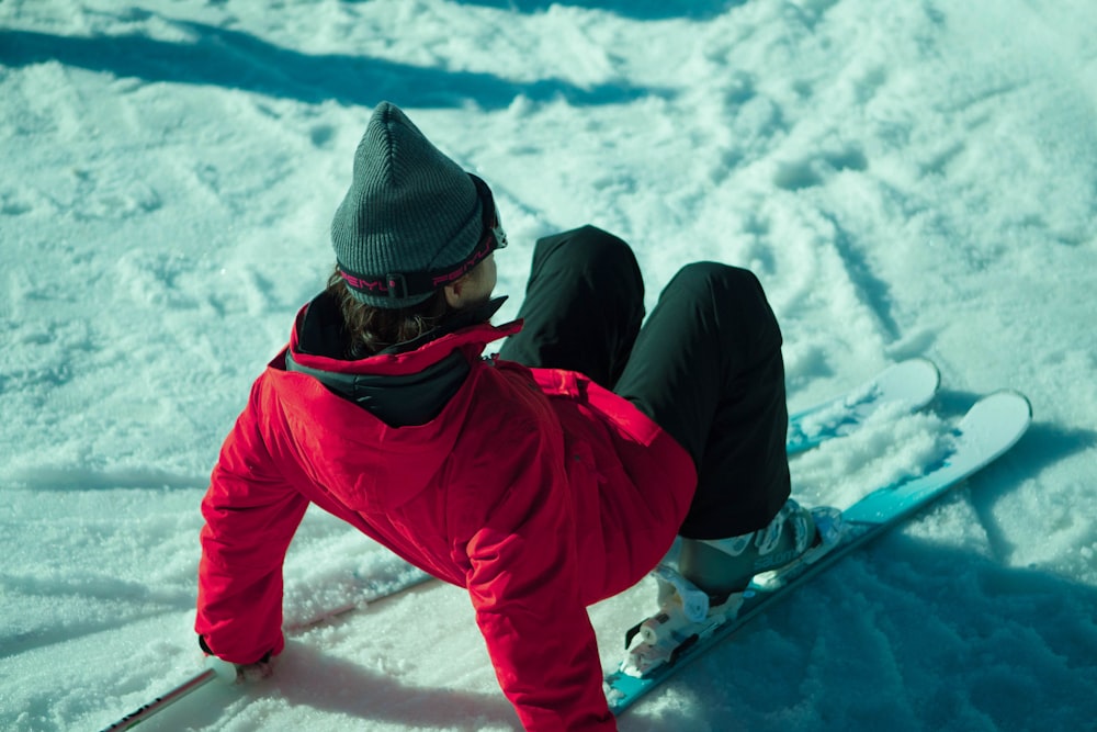 person in red jacket and black knit cap sitting on snow covered ground during daytime