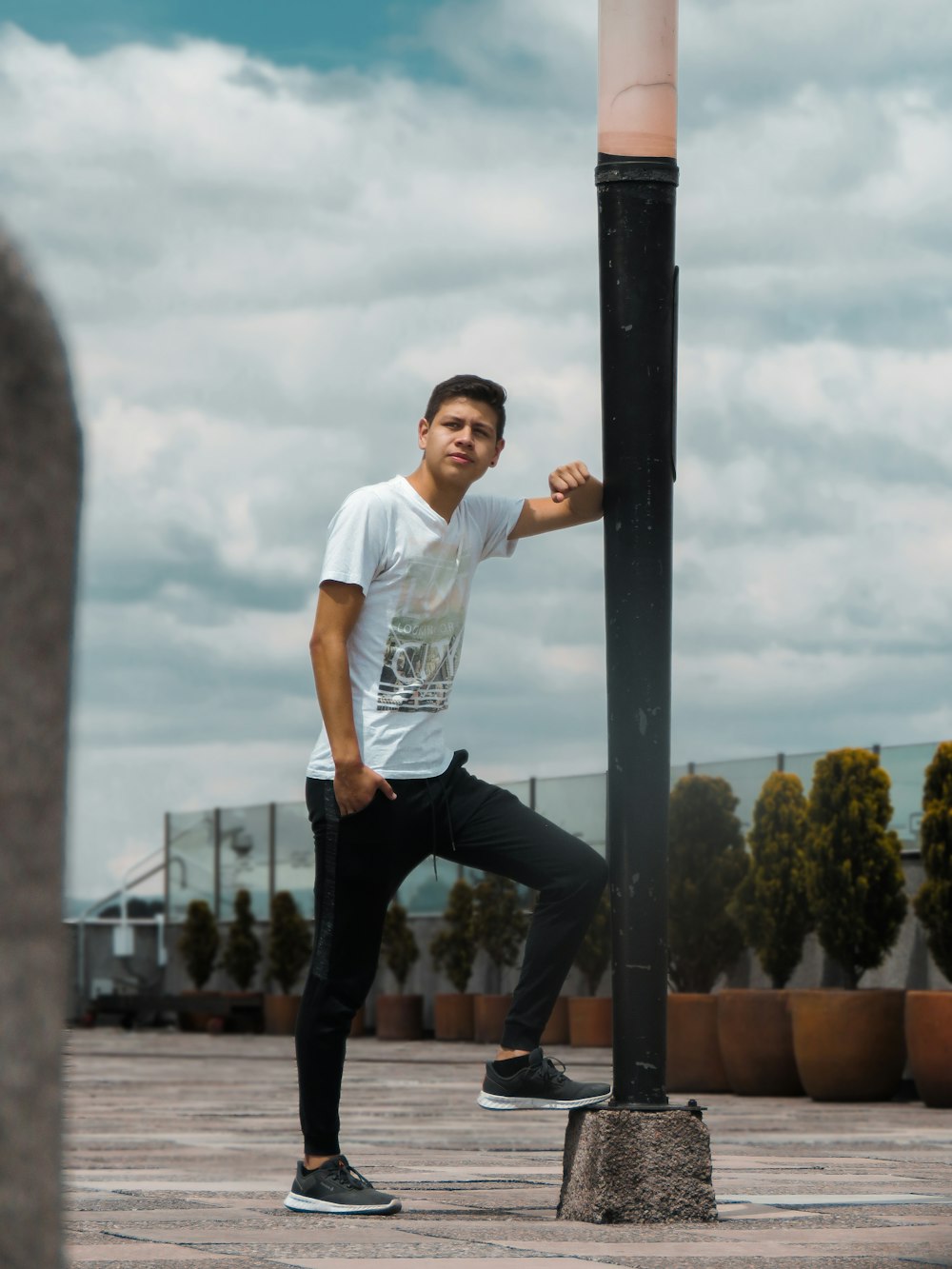 man in white t-shirt and black pants standing on black metal post during daytime