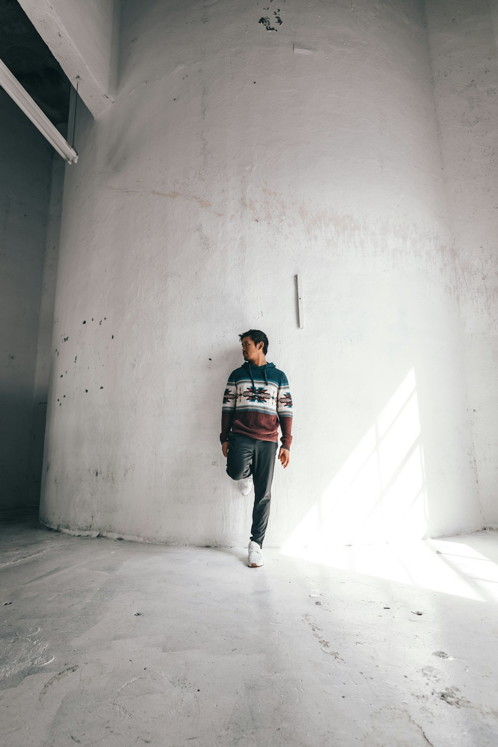 man in black and red jacket and blue denim jeans standing on white concrete floor