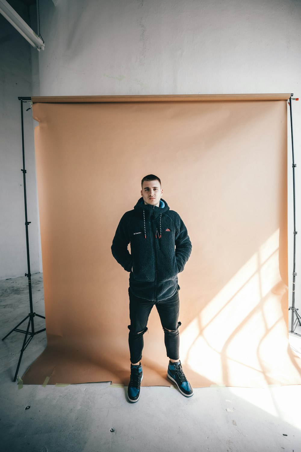 man in black jacket standing beside white wall