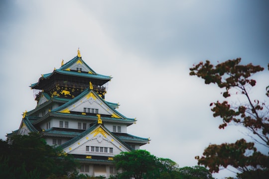 white and green concrete building under white clouds during daytime in Osaka Castle Park Japan