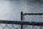 A close-up view of a chain-link fence with a metal post, overlooking a body of water that reflects sunlight.