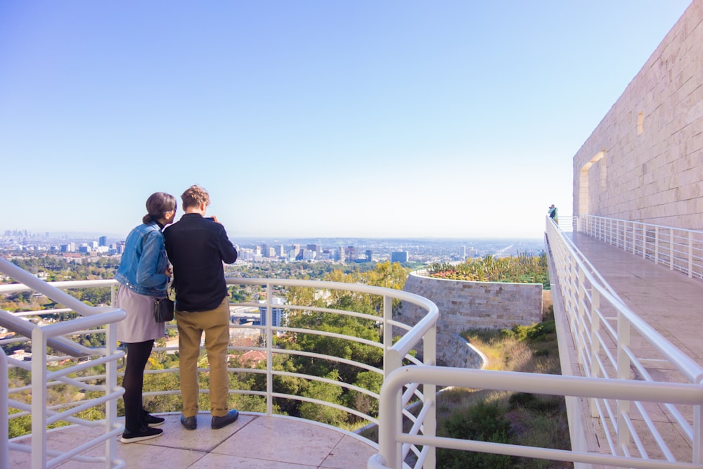 man and woman standing on top of building looking at the city during daytime