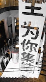 A large vertical banner with bold Chinese characters is displayed, dominating the interior space of a modern building. The architecture features dark reflective surfaces and a combination of industrial and sleek design elements.
