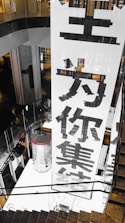 A large vertical banner with bold Chinese characters is displayed, dominating the interior space of a modern building. The architecture features dark reflective surfaces and a combination of industrial and sleek design elements.