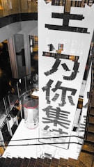 A large vertical banner with bold Chinese characters is displayed, dominating the interior space of a modern building. The architecture features dark reflective surfaces and a combination of industrial and sleek design elements.